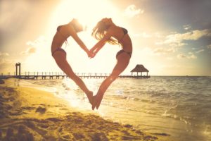 two women on the beach making a heart shape with their bodies
